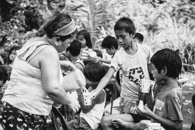 Black and white photo of a woman serving drinks to children outdoors.