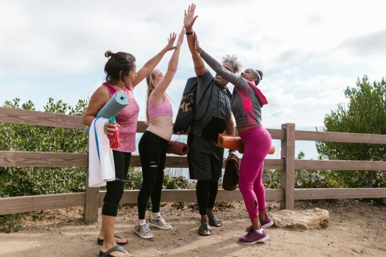 Four diverse friends in activewear high-five after an outdoor yoga class.