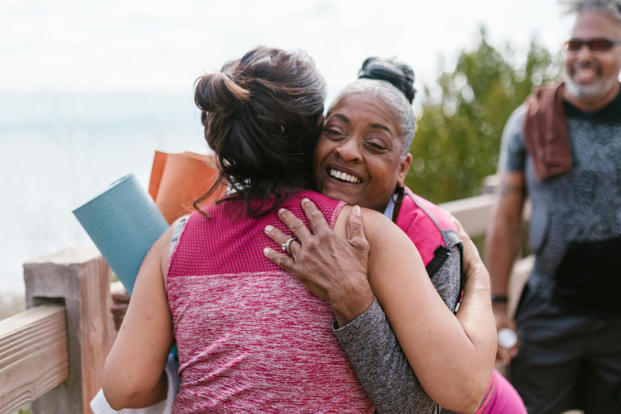 Friends embracing joyfully outdoors with yoga mats, radiating happiness and connection.