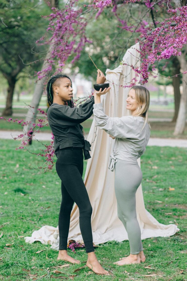 Two women practicing yoga together in a serene park setting, promoting wellness and friendship.